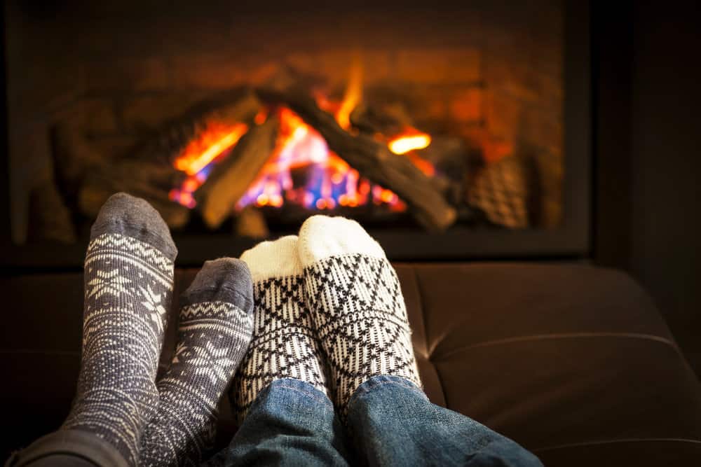 Two pairs of feet with socks in front of a fire as a couple watches romantic Christmas movies