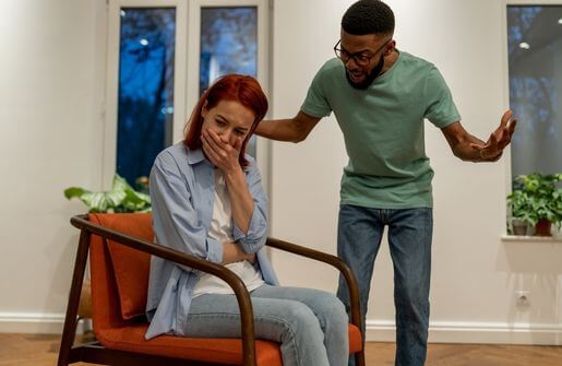 Unhappy married couple standing before a gray wall, displaying signs of discontent through their body language