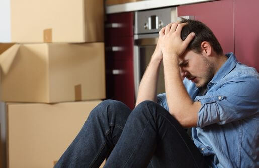 A disheartened man sits on the floor with his head in his hands, displaying signs of a broken spirit