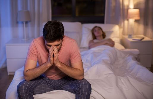 An emotionally broken man sits on the bed with his hands covering his face, displaying a sense of despair and hopelessness