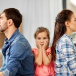 A family, with their hands on their faces, sits on the couch. The image depicts a situation where the ex-partner wants to reconcile