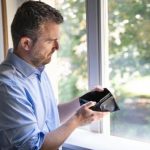 A man gazes at his wallet through a window, contemplating his financial situation in the context of dating a broke man