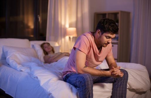 An image of a broken man sitting on a bed with his wife, both looking somber and lost in thought