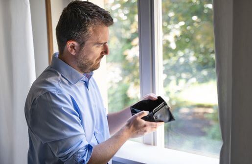 A man gazes at his wallet through a window, contemplating his financial situation in the context of dating a broke man